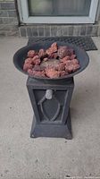 Oblique front view of the propane fire pit showing the bowl filled with red lava rocks on the black pedestal base with control knob.
