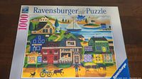 Photo showing the front of the Ravensburger puzzle box displaying the village harbor artwork and 1000-piece indication.