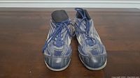 Top front view of both blue Mizuno baseball cleats on wooden surface showing laces and toe area