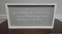 Rectangular wooden framed wall sign with white text on gray background and white frame placed on floor