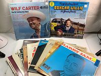 Photo showing multiple vintage LP vinyl record albums including Wilf Carter's 'How My Yodeling Days Began' and Boxcar Willie's 'King of the Road'. Several other albums are partially visible in the stack in front.