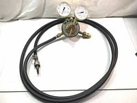 Full view of oxygen regulator with attached hose laid out flat on white surface.