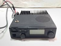 Front view of the Kenwood TK-805 UHF FM transceiver showing buttons, knobs, speaker grill, and digital display.