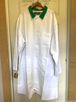 Full view of the white lab/butcher coat hanging on a hanger showing front design and green collar.