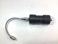 Side view of the black cylindrical signal or audio filter with attached coaxial connector and short cable with male jack plug