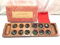 Photo showing the open wooden Mancala board inside the original box and a red fabric pouch beside it.