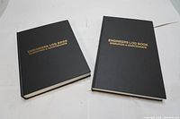 Two new Engineers Log Books with black covers, gold embossed titles 'Engineers Log Book Operation & Maintenance'.