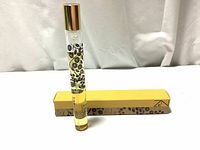 Small cylindrical perfume bottle with gold cap and black floral designs standing upright next to its yellow box labeled 'ZEN'.