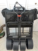 Photo of the back of the black folding beach wagon showing four wide plastic wheels, metal frame, and handle with locking mechanism.