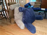 Three XXL bed husband pillows in brown, beige, and navy blue arranged on floor showing front and side views with attached rolled pillows.