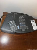 Top view of Bose Wave Radio/CD system with remote control placed on it. Visible numeric keypad, preset buttons, and playback controls. Dust visible on the surface.