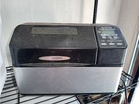 Front side view of the black and silver Zojirushi bread maker showing the control panel and brand label.
