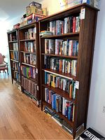 Three cherry wood bookcases side by side filled with books
