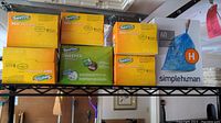 Photo of the entire lot of cleaning supplies including Swiffer 360 Dusters, Swiffer Sweeper cloths, and SimpleHuman trash bags on a shelving unit.