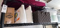 Shelf with cleaning supplies including Clorox wipes in box, laundry detergent jugs and storage bins