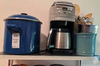 Shelf view of blue enamel pots, coffee maker and utensil holders