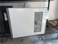 White Hampton Bay automatic dehumidifier on metal shelf, showing front with control window and knob, some dust visible.