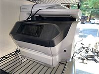 HP OfficeJet Pro 8740 printer copier resting on metal shelving with visible touchscreen control panel and paper trays.