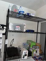 Wide view of black wire shelving with various kitchen items including boxed Nutribullet blender, Ninja appliances, and plastic containers.