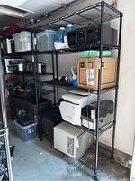 Side view showing full height and four shelves of one black metal wire shelving rack with castors. Various household and office items shown on shelves (not included).