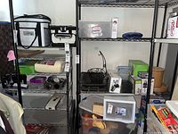 Photo showing the taller black metal utility shelving unit and part of shorter chrome wire shelving with various household items stored on shelves, including boxes and containers.