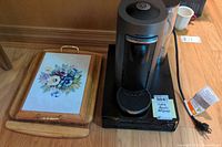 Nespresso Virtuo coffee maker next to a wooden cutting board with a floral ceramic tile inset.