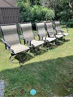 Front angle view of all four patio chairs side by side on grass, showing the seating and armrest design