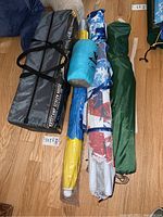 Photo showing the Browning Basecamp screen house tent bag alongside three rolled beach umbrellas in various carrying cases.