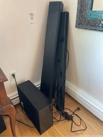 Photo of Samsung Harman/Kardon HW-Q60R and Samsung HW-J650 soundbars and subwoofers setup leaning against wall on hardwood floor, connected with wires visible.