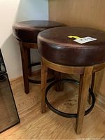 Two swivel stools with wooden legs and brown vinyl cushioned seats placed on hardwood flooring.