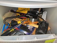 Top view of plastic storage container filled with various hand tools including screwdrivers, wire, crowbar, lock packaging, and yellow DeWalt tool cases.