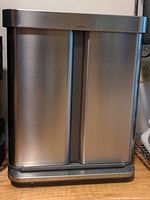 Front view of a double sided stainless steel trash bin by Simplehuman.