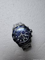 Close-up of large Invicta diver watch with blue dial and metal bracelet on white background.