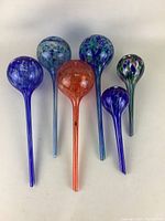 Full set of six glass watering bulbs in various colors and patterns arranged on flat surface.