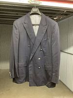 Full front view of navy blue double-breasted men's blazer hanging, showing button details and general wear.
