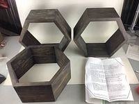 Three dark stained solid wood hexagon display shelves shown standing on a white surface with mounting instruction sheet nearby