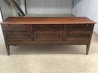 Front view of dresser showing six drawers with round wooden knobs on flat concrete floor.