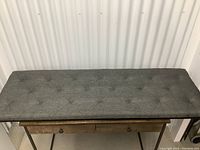 Full top view of the upholstered gray bench top on a wooden base with drawer knobs visible below.