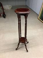 Full view of dark stained, solid wood display stand with round top and spindle legs on a concrete floor.