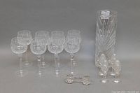 Full lot: 8 Bohemian cut crystal wine glasses, 4 cut crystal vases, salt and pepper shakers, and cutting utensil rest arranged on a table.