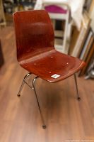 Front angled view showing reddish-brown molded seat with wood grain texture and four chrome metal legs with capped feet.