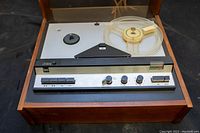 Front angle showing the tape recorder with one reel, wooden casing, and control buttons visible.