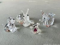 Four Swarovski miniature crystal animal figurines (dog, snail, koala, elephant) arranged side by side on a flat surface.