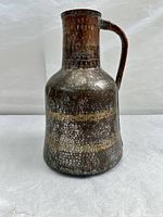 Front view showing overall jug shape, handle, and textured surface with aged patina.