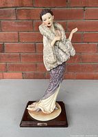 Full view of the Art Deco lady figurine on wood base with brick background.