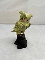 Front view of green serpentine owl sculpture with red gemstone eyes standing on black carved soapstone base.