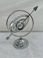 Front view of the modern astrolabe armillary sphere showing polished circular rings and central arrow detail.
