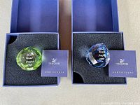 Top-down view of both crystal paperweights placed in their original blue boxes along with their certificates.