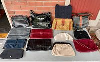 Overview of all 13 vintage purses laid out on a table with a brick wall background, showing variety of materials and styles.