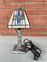 Photo of vintage stained glass table lamp showing the front view with stained glass shade and metal base, cord visible